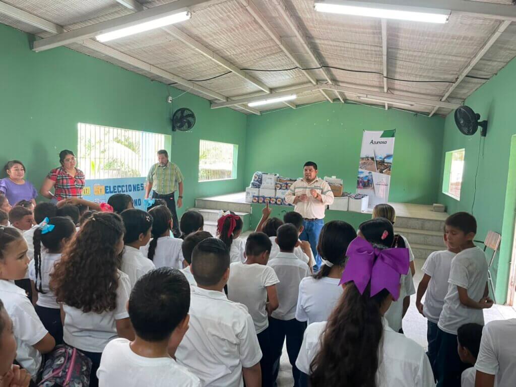 Equipo de Asuntos Corporativos de Azunosa junto a maestros y 250 estudiantes de la Escuela El Porvenir sosteniendo empaques de alimento MannaPack en Aldea El Bálsamo.